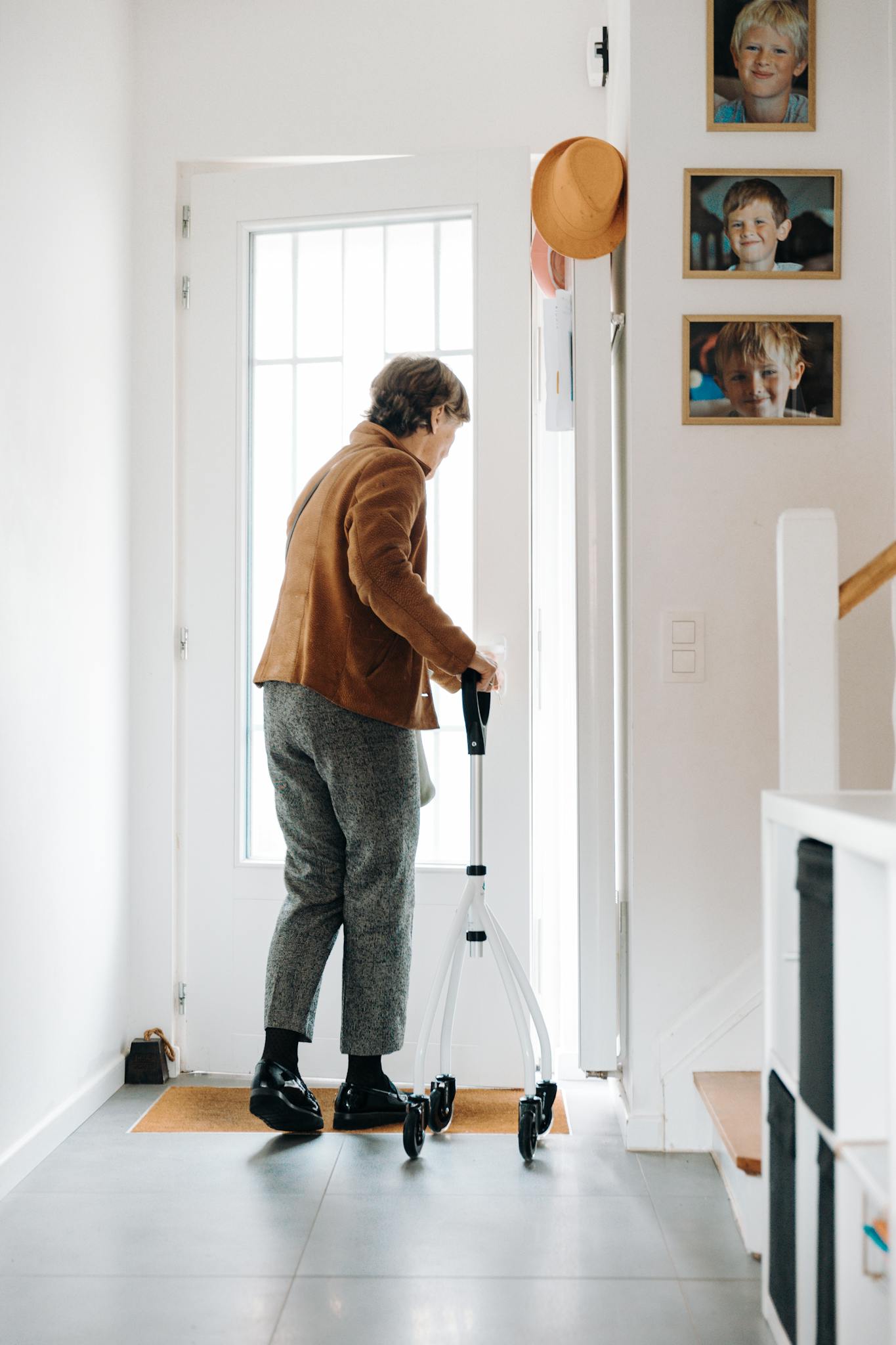 An elderly woman using a rollator to exit her home, capturing daily life.